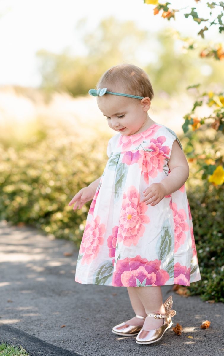 baby-walking-silk-floral-summer-dress-wearing-blue-bow-and-rose-gold-shoes
